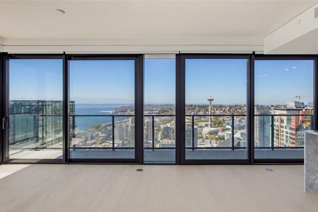 Space Needle and Elliott Bay through the window wall of the empty living room at First Light Residence 4504